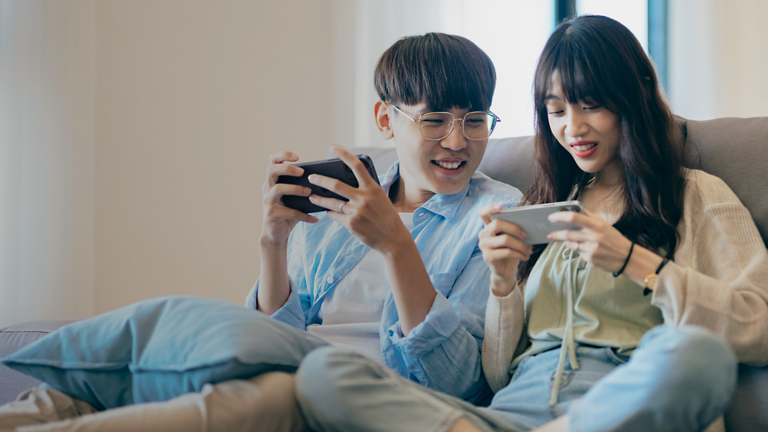 Two people sitting on a couch playing games on their iPhones.