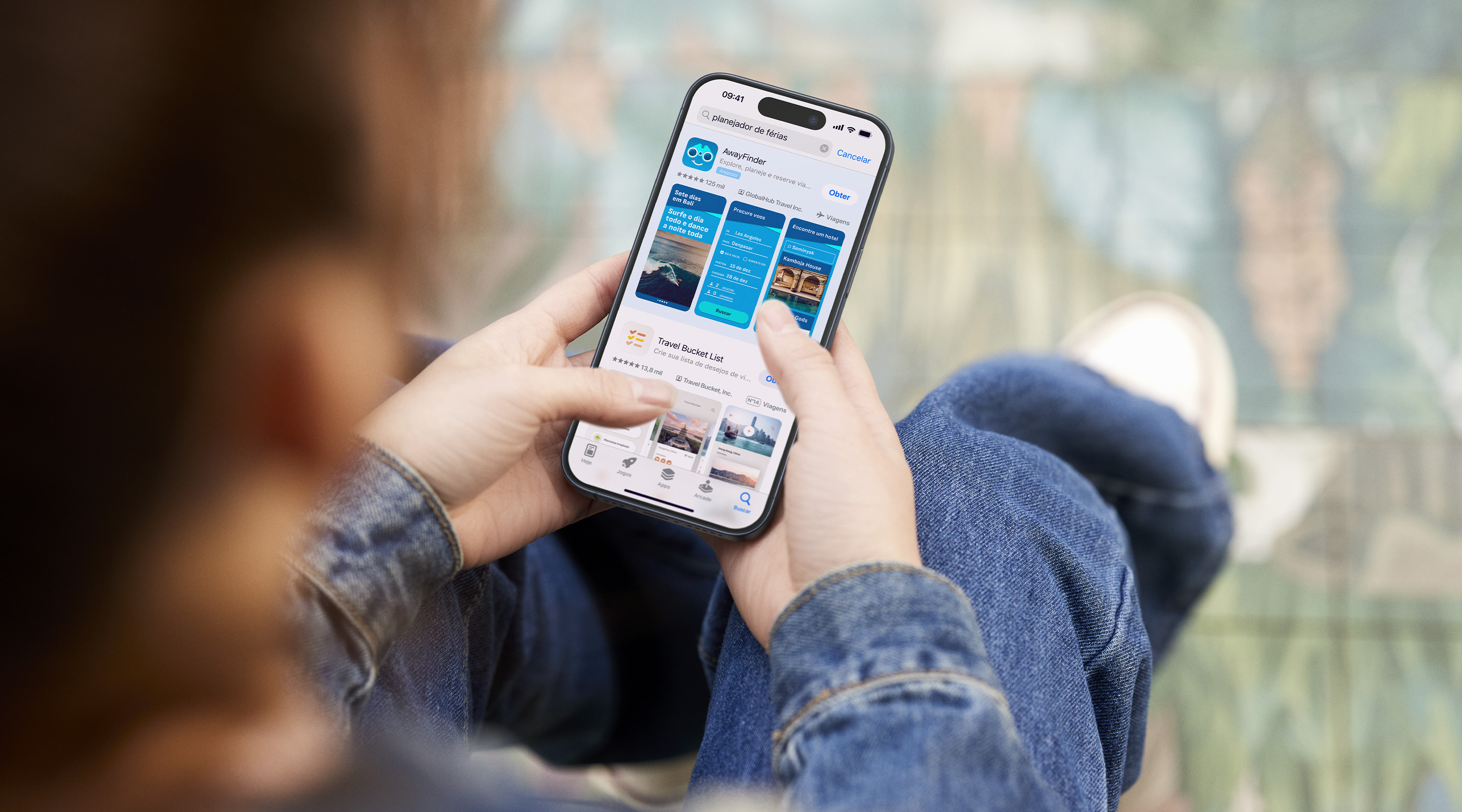 Duas mãos segurando um iPhone. A App Store está aberta em um anúncio de resultados de busca para o app de exemplo, AwayFinder, com o termo "planejador de férias" inserido na caixa de busca.