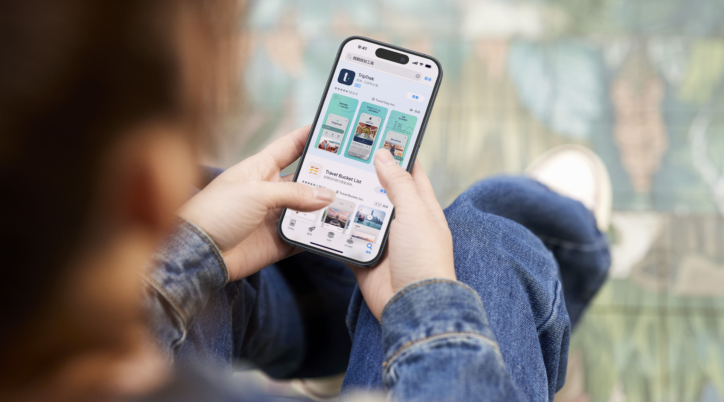 双手拿着 iPhone。已打开的 App Store 展示了示例 app“TripTrek”的搜索结果广告，搜索框中输入了“假期规划工具”一词。