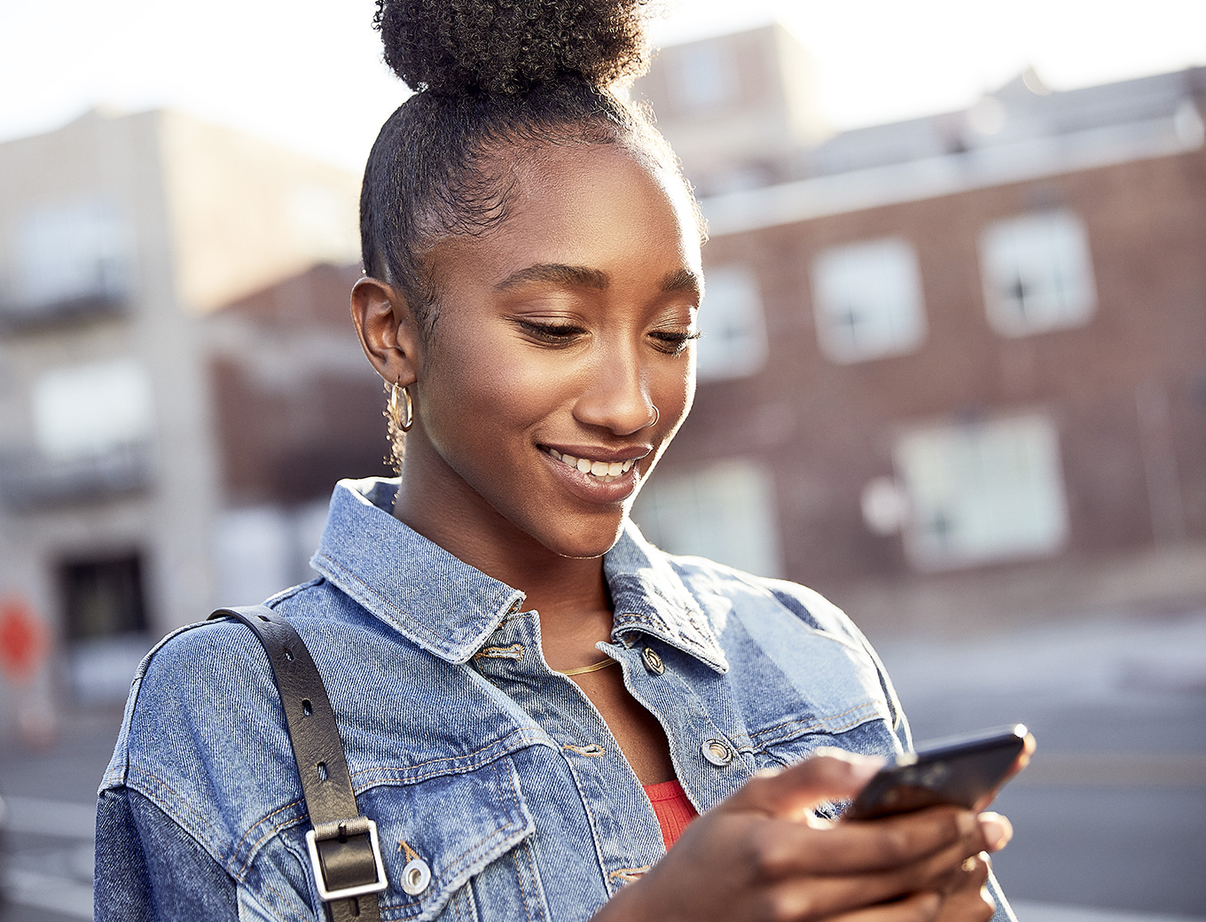 Une femme sourit en regardant l’écran d’un iPhone qu’elle tient. 