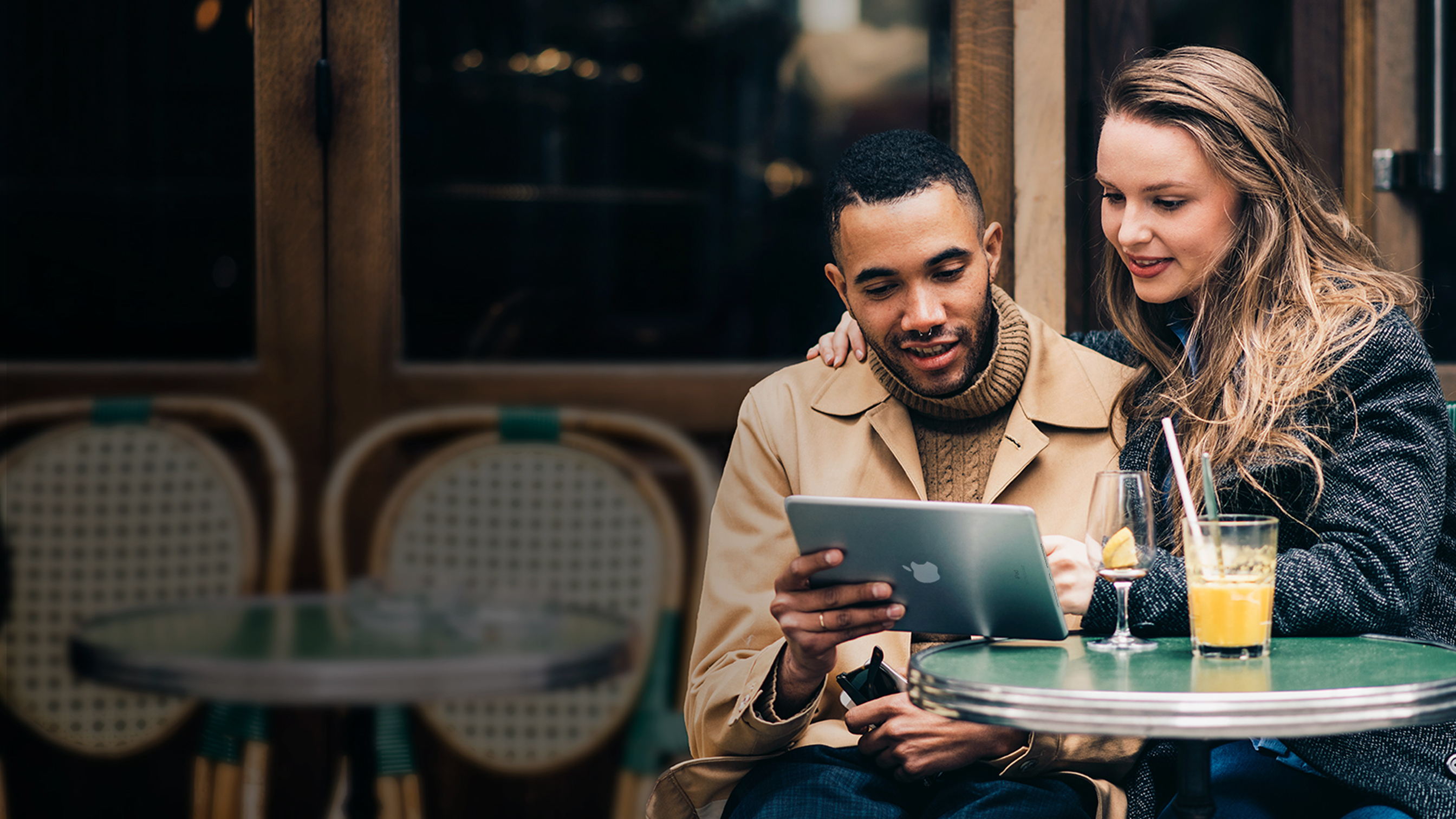 Dos personas sentadas en una cafetería, mirando juntas un iPad.