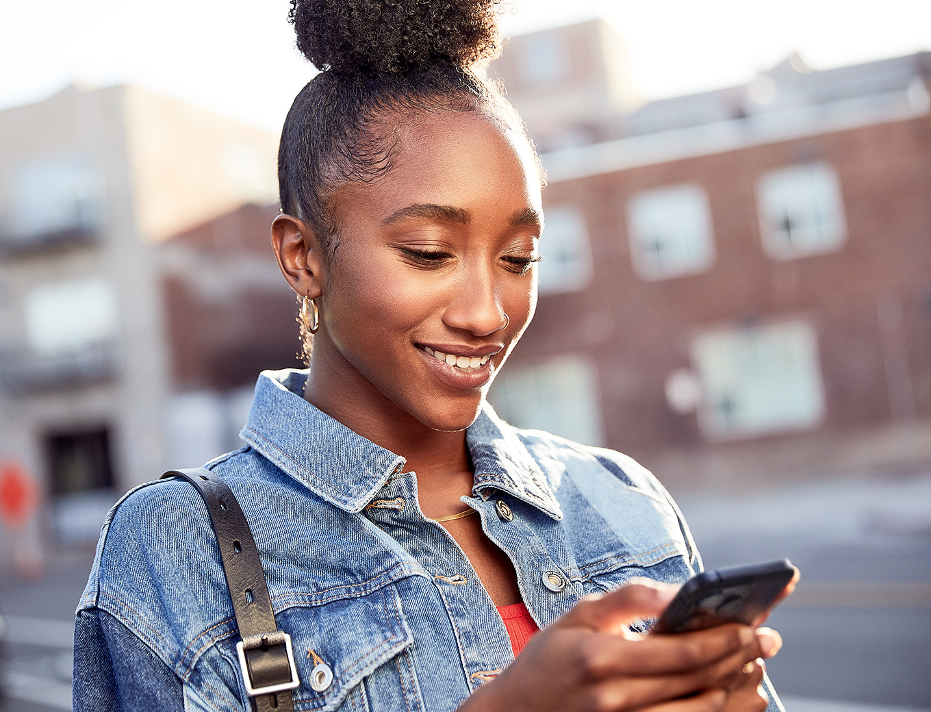 Una mujer sonriente mirando la pantalla de un iPhone que está sosteniendo. 